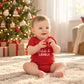 Bambina con body rosso personalizzato per il primo Natale davanti all’albero di Natale