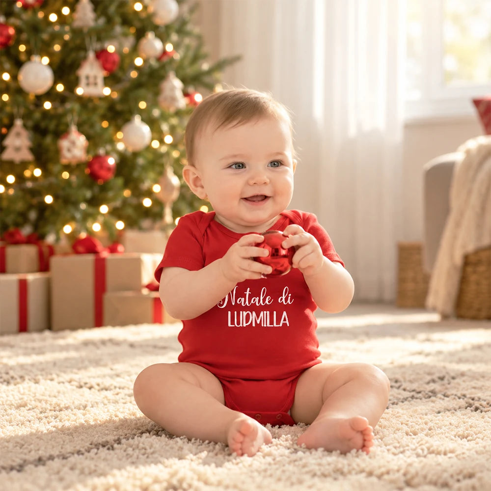 Bambina con body rosso personalizzato per il primo Natale davanti all’albero di Natale