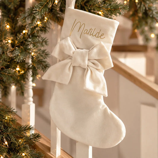Calza di Natale avorio personalizzata con nome in oro e grande fiocco appesa vicino all’albero