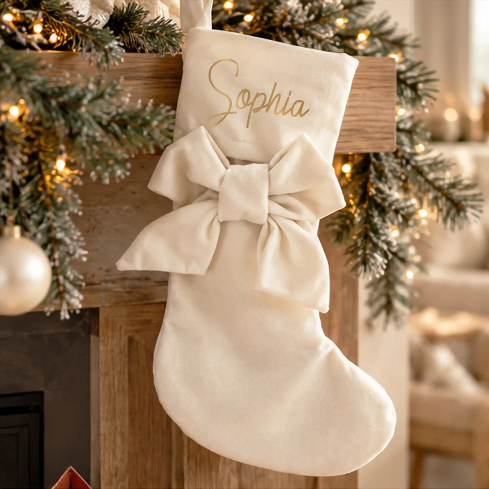 Calza di Natale avorio personalizzata con nome in oro e fiocco, appesa in un ambiente natalizio