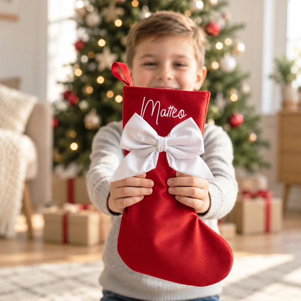Calza di Natale rossa personalizzata con nome e fiocco bianco in mano a un bambino