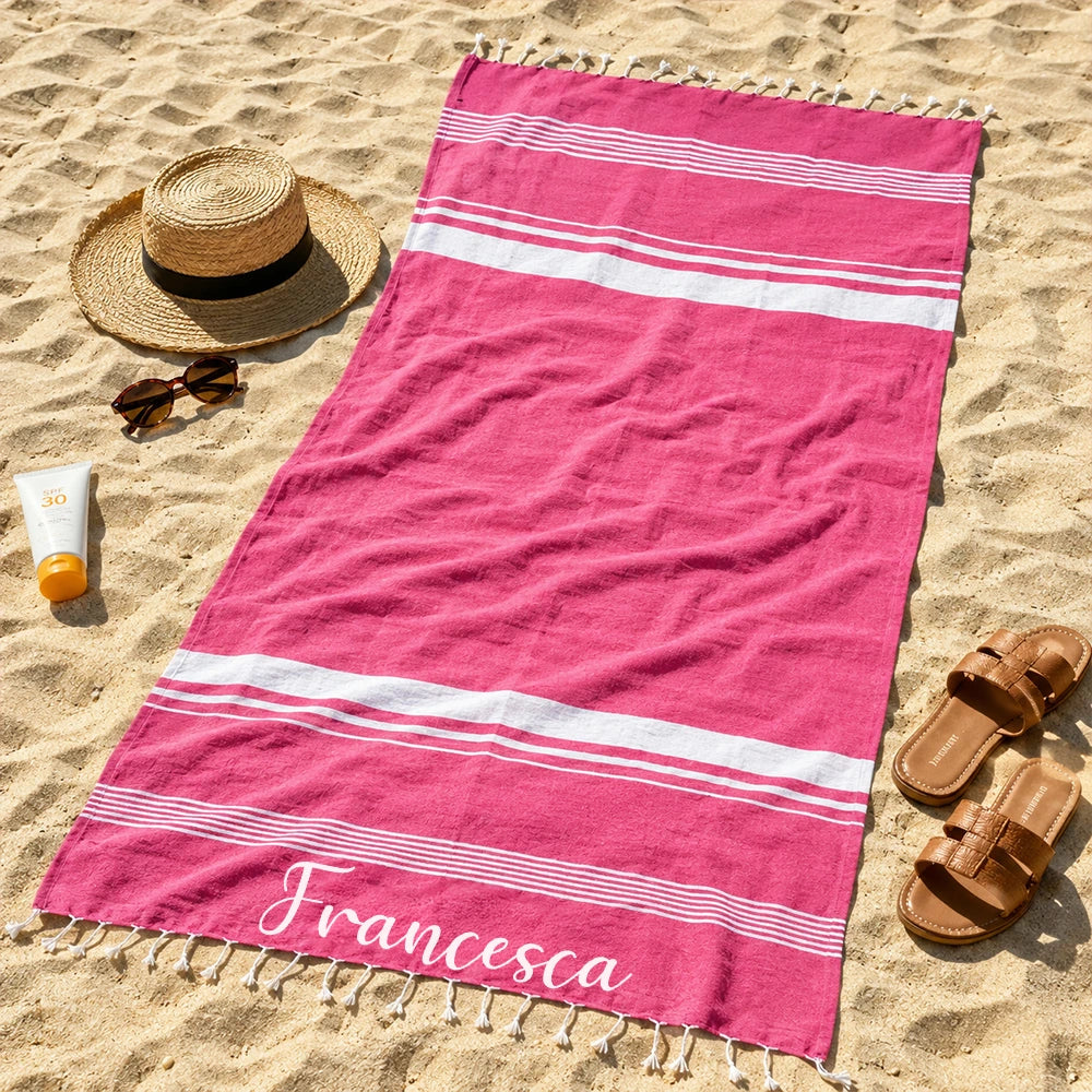 Pareo telo mare fucsia personalizzato con nome bianco steso sulla sabbia